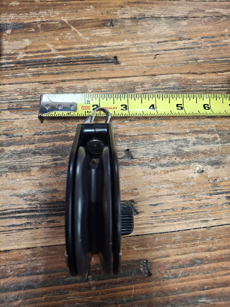 Black pulley side view on a wooden surface with a tape measure for scale.