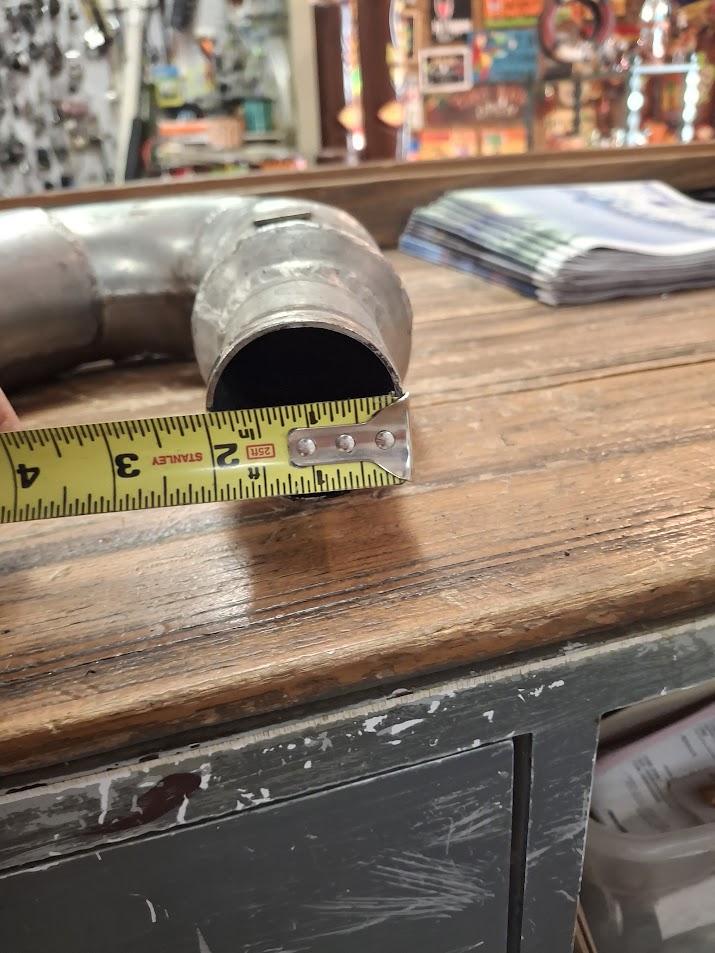 Metal pipe with a measuring tape showing its diameter on a wooden surface.