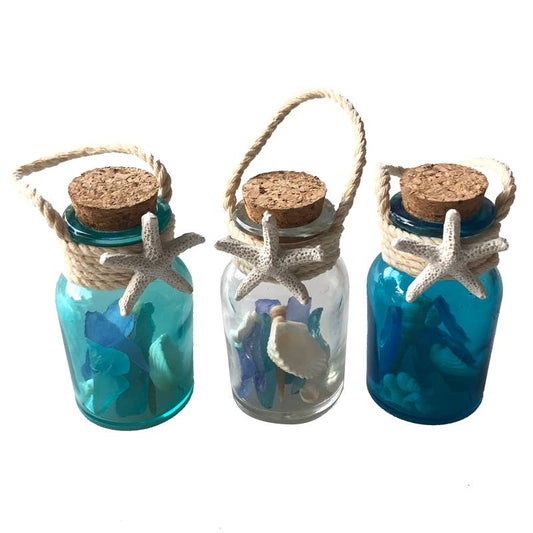 Three decorative glass jars with cork lids, starfish, and seashells on a white background