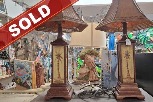 Two wooden lamps with wicker shades on a table in a store setting.