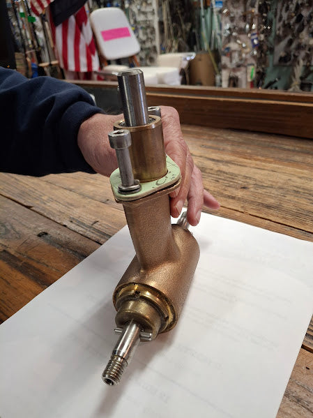Person holding a brass bow thruster gear box on a wooden table with an American flag in the background.