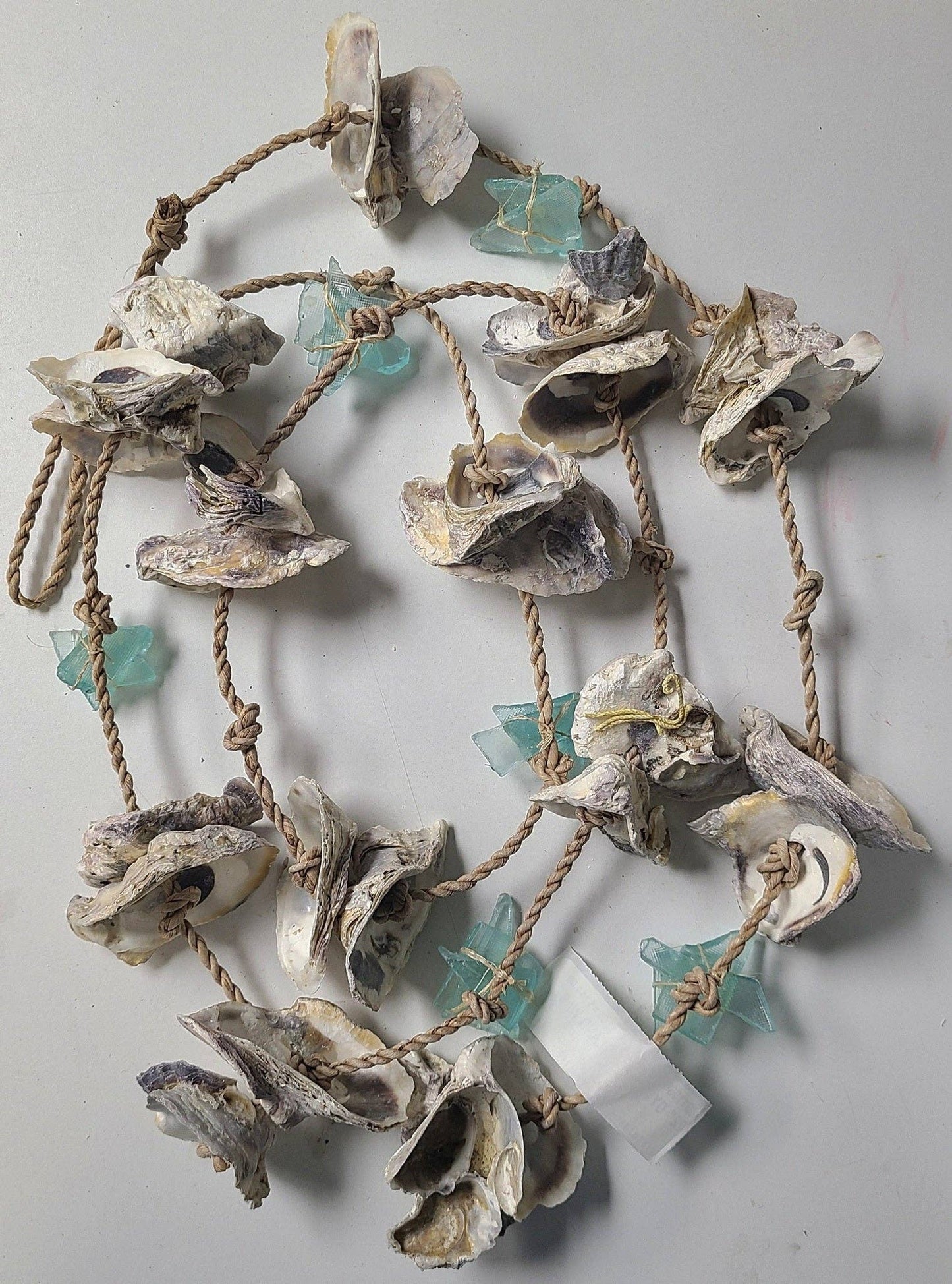 Decorative wall art made of shells, sea glass and rope on a plain background