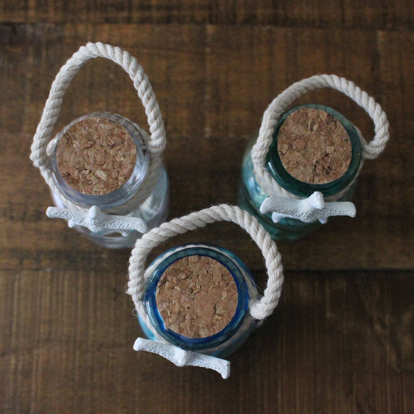 Three glass jars with cork lids and rope handles on a wooden surface